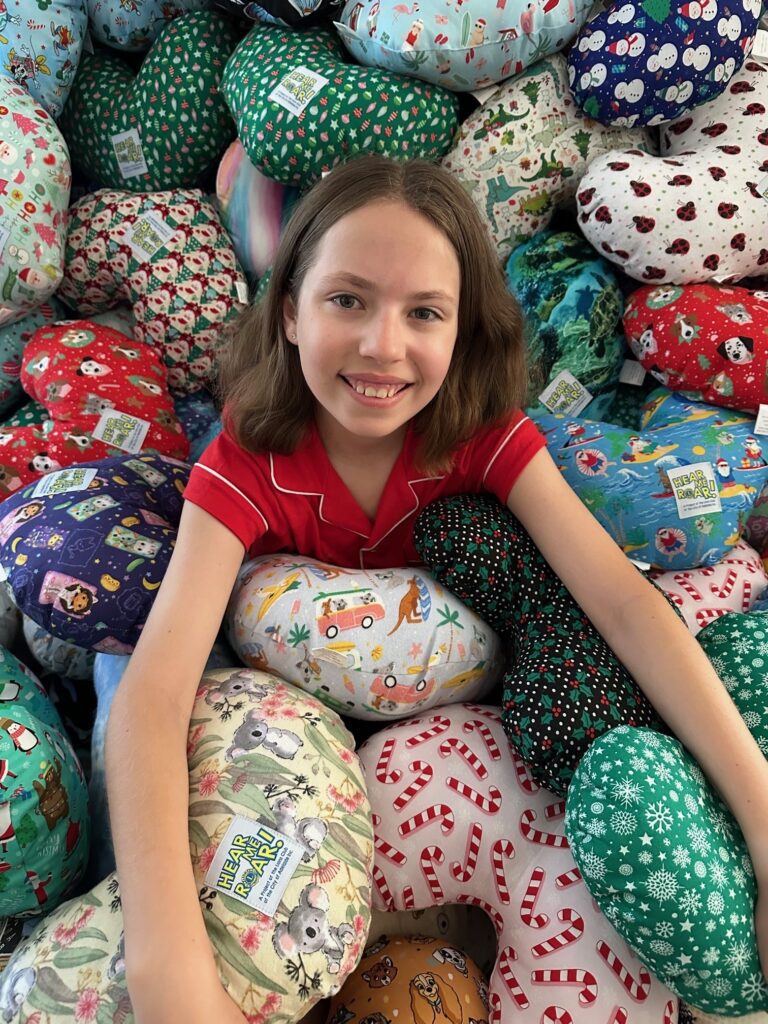 Addie in a pile of handmade cushions by the Hear Me Roar! Project